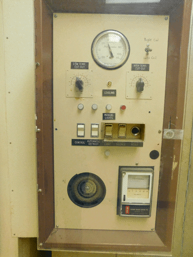 Beige climate-control panel behind plastic or glass with various switches, buttons, knobs, and circular thermometer meter, manufactured by Norman Bragar Company of Newark, NJ