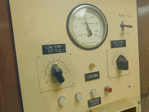 Close up of top half of the control panel with (top to bottom, left to right) the thermometer meter, toggle switch with handwritten labels "Right Coil" and "Left Coil," chickenhead knob on square base plate with label "LOW TEMP. CUT-OUT," yellow light labeled "Cooling," chickenhead knob labeled "HIGH TEMP. CUT-OUT," three white lights and a red labeled "MANUAL LIGHTS"