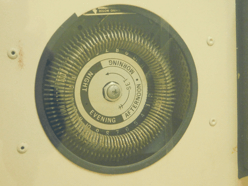 Close-up of the aforementioned "some sort of coil," with an upside-down label on the top revealing it is actually the "TIMING MOTOR." The central plate has, center outwards, the word "SET" in a CCW arrow, a ring containing the words "NIGHT" and "EVENING" on black and "AFTERNOON" and "MORNING" on white, and a ring labeled with the hours of the day, somewhat obscured by the thin radial slats that made me think this was some sort of coil.