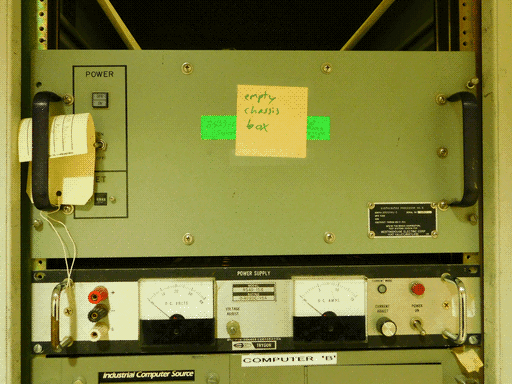 The top portion of an assembly, labeled on its upper panel by scotch-taped sticky note "empty chassis box." This is on top of an older bright green, partially obscured label. A plaque also labels the upper panel of the assembly (same as the sticky note is on) "DISTRUBUTED PROCESSOR NO. 2," manufactured by THE BENDIX CORPORATION, TEST SYSTEMS DIVISION for WESTINGHOUSE ELECTRIC CORP of HUNT VALLEY, MARYLAND. Not sure how it got here. This upper plate has a power and reset switch and two black handles and that's pretty much it. Underneath this plate is a power supply with two rectangular meters measuring DC volts and amps, each with an adjustment knob, and ports for ground, positive and negative voltage. Just below the power source, the very top of another module is visible, labeled "COMPUTER 'B'" and "Industrial Computer Source."