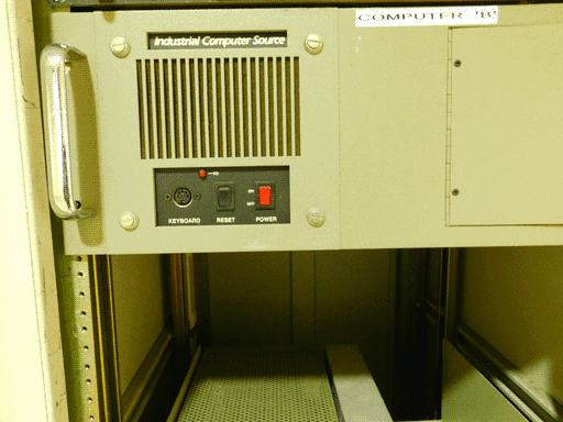 Here we see the whole "Computer 'B'" module. Actually a bit of the right end is out of frame but probably there was nothing there. There's a vent on the left, then below that a small black recessed plate with a KEYBOARD port (I think it would be a PS/2, but it's got 5 prong holes plus a little slot at the bottom?? That doesn't look right), reset switch, red POWER switch, and a little red light labeled "HD." On the right end of the module, the hinges and left half of, presumably, a hatch are visible. Below this module is the inside of the chassis.