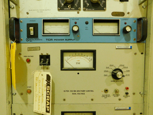 Here we see the very bottom of the latter module in the last image, and two more full modules. The top is narrower and a sort of pastel azure, a TCR POWER SUPPLY made by ELECTRONIC MEASUREMENTS INC. As expected it has a DC voltmeter and ammeter and voltage and current control knobs. Below it is a wider off-grey ULTEK 350 MA ION PUMP CONTROL, DUAL VOLTAGE made by PERKIN-ELMER. It has a P-E pressure meter in Torr (noted in orange) with a black 0-20 linear and orange (a bit over) 10^-9 to 10^-5 logarithmic scale. That's a bit confusing. It's got a RANGE SELECTOR knob and some sockets, and a circuit breaker-looking power switch with a white tag tied on it reading XSCRAP, very ineffectively scribbed out, with HOLD written underneath, then further details. There are also a few lights and sockets. At the very bottom of the image the top of another PERKIN-ELMER module of the same color is visible.