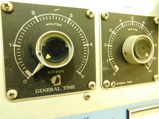 Close-up of the pair of smaller knobs on the SUBLIMATION POWER SUPPLY. They are mounted on black, rounded square base plates with 0-5 (left) and 0-10 (right) minute scales. Each plate reads GENERAL TIME on the bottom, and the left knob says HAYDON right above that. The knobs themselves are round, ridged and pale grey with pointers sticking out, topped with black discs with a little yellow triangle marker on each of their edges, aligned with the pointer. That's kind of overkill in my opinion, unless the black discs are actually  separate knobs on top of the main knobs?