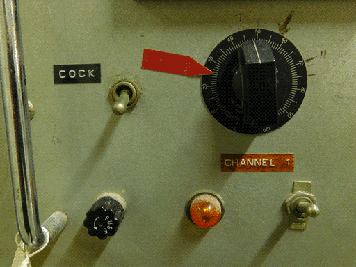 Close-up of some controls on the aforementioned lighter grey panel with the two Simpson meters. The left-hand (CHANNEL 1) knob has a 0 - 100 scale on its round base plate, both ends near the bottom, with a red sticker on the panel and plate approximately marking 25. To the left of the knob is that COCK toggle switch, and below the knob and COCK, the fuse, orange light, and other toggle. 