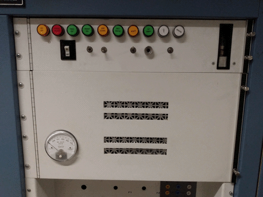 The top right control panel in the assembly. There's a row of colored indicator lights on top, then an on switch, a few toggle switches, a vertical rectangular slot with unclear metallic objects in it, a round Triplet 0-1000 voltmeter, and four horizontal slots exposing sheet metal with a tiled square-split-into-eight-triangles pattern cut into it. Below the panel, the top of a concave area is visible.