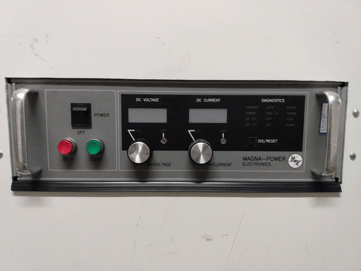 Close-up of grey Magna-Power Electronics power supply in the left of the assembly, with metal handles on either side, and between them, a power switch, stop and start buttons, DC voltage and current knobs and displays, a bunch of labels for diagnostic lights (i presume, but the lights are not visible off), and a square button labeled "DIS/RESET."